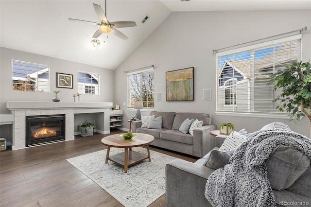 living room featuring visible vents, wood finished floors, high vaulted ceiling, a tiled fireplace, and a ceiling fan
