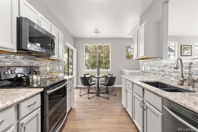 kitchen with appliances with stainless steel finishes, tasteful backsplash, light stone countertops, a sink, and light wood-style flooring