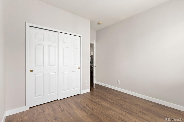 unfurnished bedroom featuring dark wood-type flooring, baseboards, and a closet