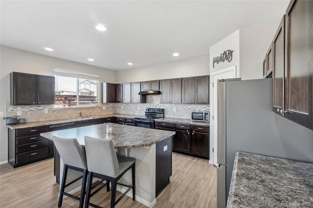 kitchen featuring decorative backsplash, appliances with stainless steel finishes, a breakfast bar, light hardwood / wood-style flooring, and a kitchen island