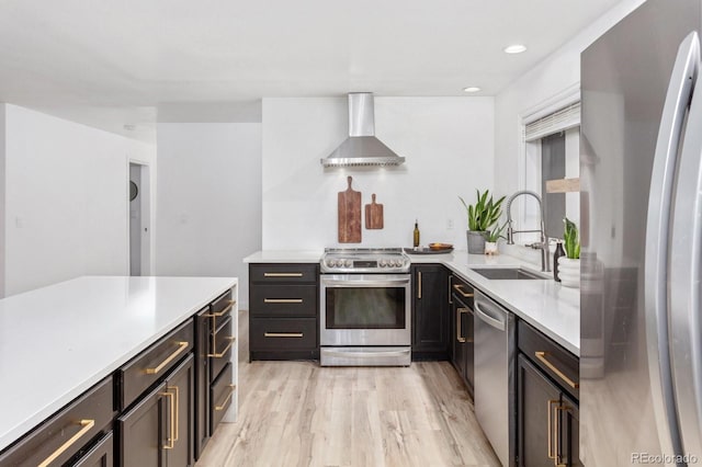 kitchen with light wood finished floors, light countertops, appliances with stainless steel finishes, a sink, and wall chimney range hood