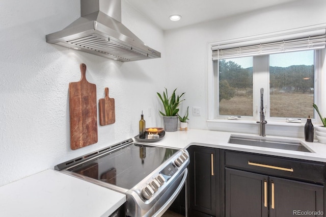 kitchen featuring light countertops, a sink, electric range, and wall chimney exhaust hood