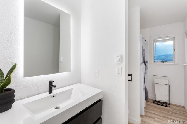 full bath with a shower with shower curtain, wood finished floors, vanity, and baseboards