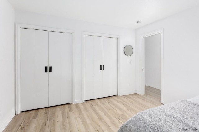 bedroom featuring baseboards, two closets, and wood finished floors