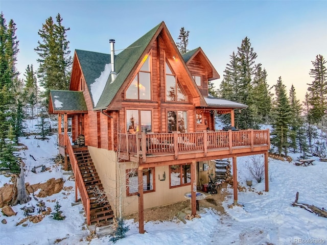 snow covered rear of property featuring stairs, a deck, and roof with shingles