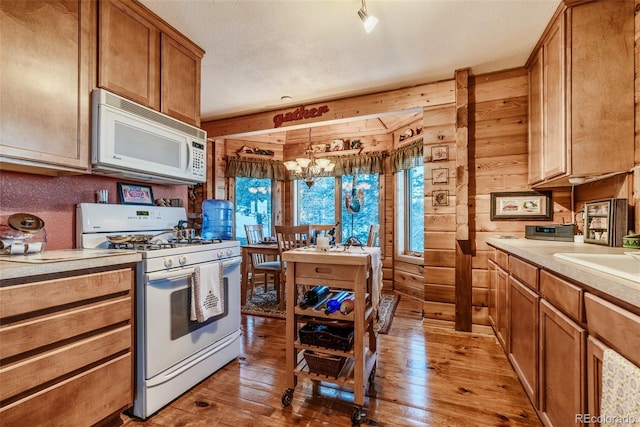 kitchen with white appliances, wood walls, light wood-style floors, light countertops, and an inviting chandelier