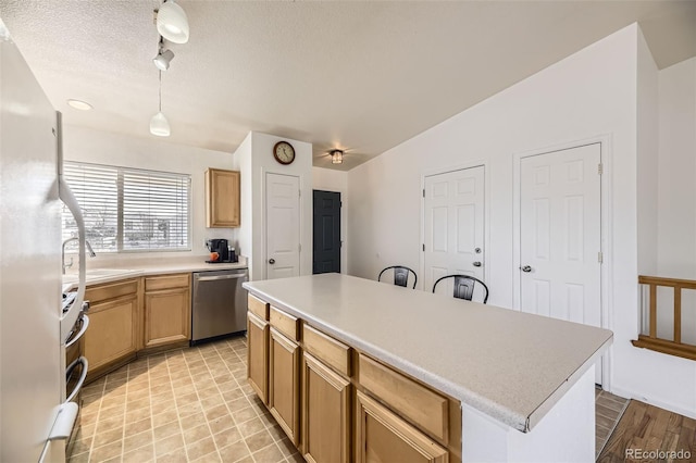 kitchen with a textured ceiling, a sink, light countertops, appliances with stainless steel finishes, and a center island