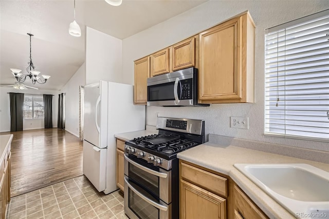 kitchen with a chandelier, stainless steel appliances, a sink, light countertops, and pendant lighting