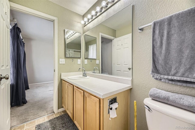 bathroom featuring toilet, a textured wall, baseboards, and vanity