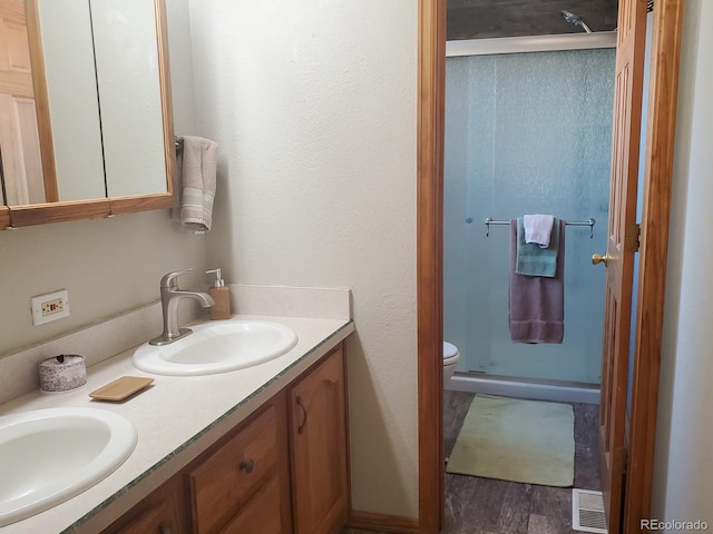 bathroom with hardwood / wood-style flooring, vanity, toilet, and a shower with shower door