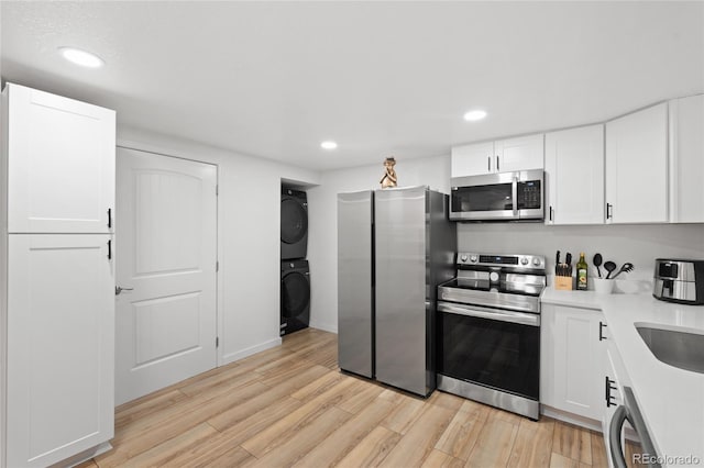 283 Leonard Ln, Northglenn, CO 80233 - kitchen with appliances with stainless steel finishes, stacked washing machine and dryer, light wood-type flooring, white cabinetry, and recessed lighting