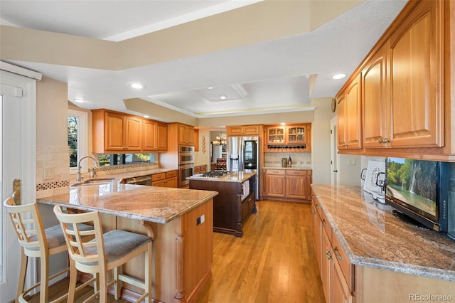 kitchen with light stone countertops, a center island, light hardwood / wood-style flooring, a tray ceiling, and a kitchen bar