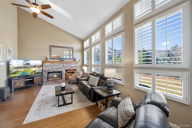 living room featuring hardwood / wood-style floors, high vaulted ceiling, ceiling fan, and a stone fireplace