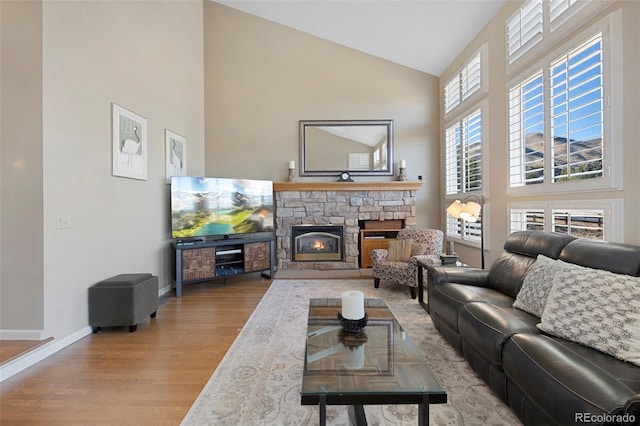 living room featuring a stone fireplace, light hardwood / wood-style flooring, and high vaulted ceiling