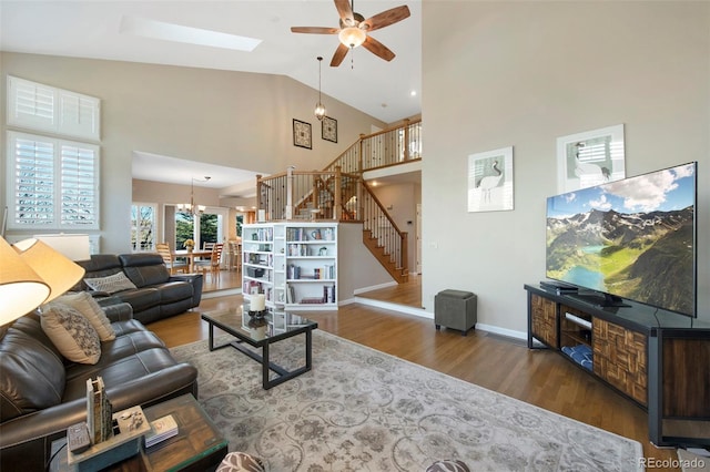 living room with ceiling fan with notable chandelier, a skylight, high vaulted ceiling, and dark wood-type flooring