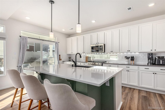 4104 N Picadilly Ct, Aurora, CO 80019 - kitchen featuring stainless steel appliances, tasteful backsplash, wood finished floors, a kitchen island with sink, and recessed lighting