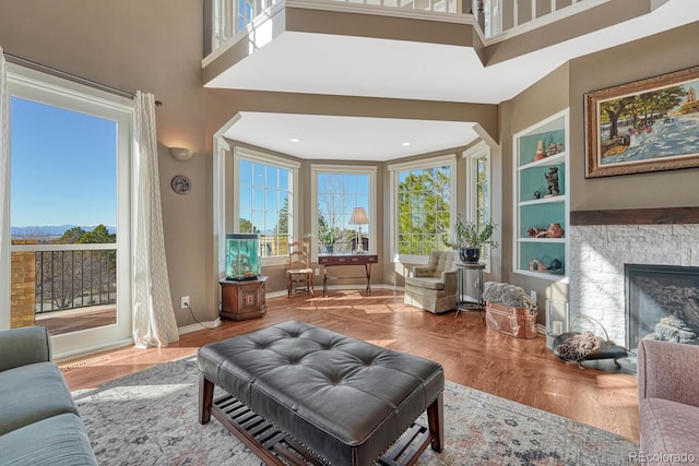 interior space with a fireplace, wood finished floors, a towering ceiling, and a healthy amount of sunlight