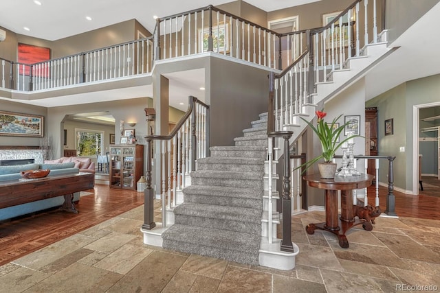 stairway with a high ceiling, a fireplace, baseboards, and stone tile flooring