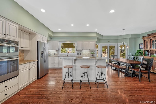 kitchen with dark wood-style floors, appliances with stainless steel finishes, white cabinetry, and decorative backsplash