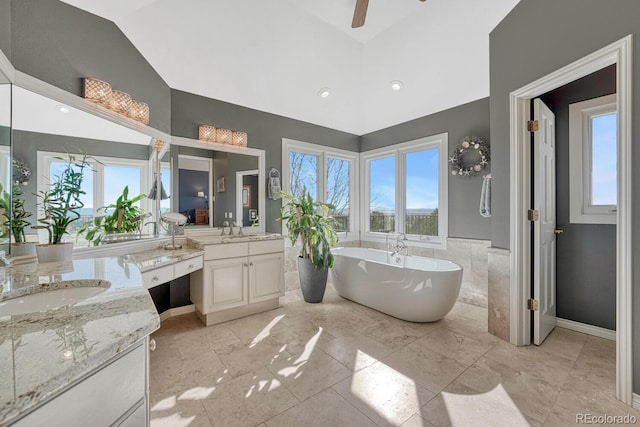 full bathroom with a ceiling fan, a sink, vaulted ceiling, a freestanding bath, and two vanities