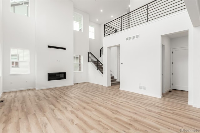 1826 Hickory Ave, Erie, CO 80516 - unfurnished living room featuring stairway, a high ceiling, light wood finished floors, recessed lighting, and a glass covered fireplace