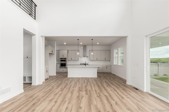 1826 Hickory Ave, Erie, CO 80516 - kitchen featuring wall chimney range hood, a high ceiling, light countertops, light wood-style floors, and gray cabinets