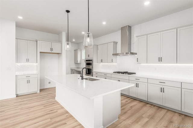1826 Hickory Ave, Erie, CO 80516 - kitchen with wall chimney exhaust hood, appliances with stainless steel finishes, backsplash, light wood finished floors, and a kitchen island with sink