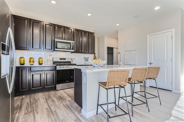 kitchen featuring a kitchen bar, a center island with sink, light hardwood / wood-style flooring, appliances with stainless steel finishes, and decorative backsplash