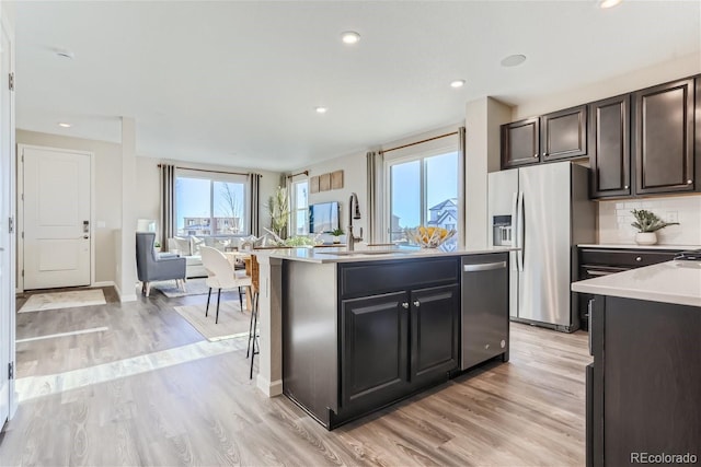 kitchen featuring appliances with stainless steel finishes, tasteful backsplash, sink, a center island with sink, and light hardwood / wood-style flooring