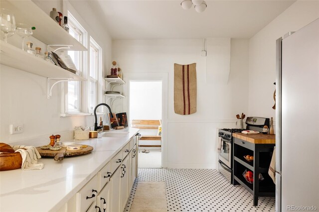 321 Fox St, Denver, CO 80223 - kitchen with freestanding refrigerator, stainless steel gas range, open shelves, a sink, and white cabinetry