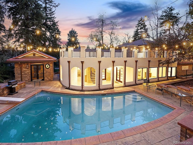 pool at dusk featuring an outdoor pool, a patio, grilling area, and a diving board