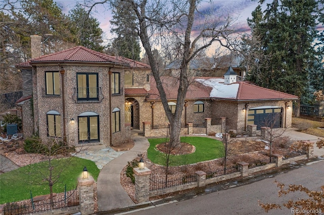 mediterranean / spanish-style house featuring driveway, a tile roof, a lawn, and an attached garage