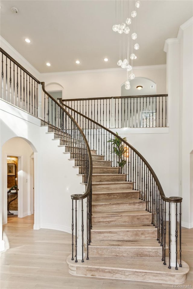 stairs featuring arched walkways, a high ceiling, wood finished floors, baseboards, and ornamental molding