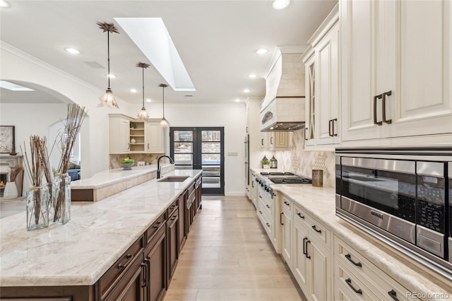 kitchen featuring open shelves, light stone counters, a sink, and pendant lighting