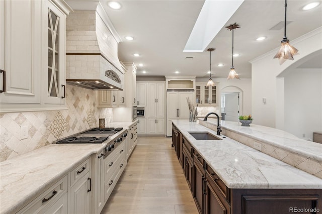 kitchen with glass insert cabinets, built in appliances, dark brown cabinets, pendant lighting, and a sink