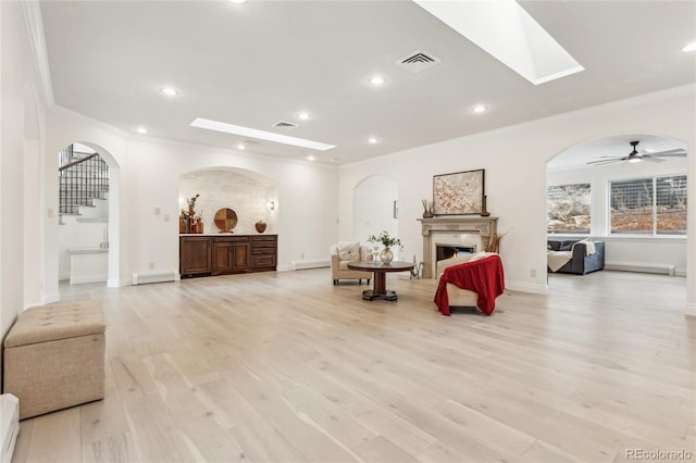 living area featuring stairs, a lit fireplace, ornamental molding, and light wood-style flooring