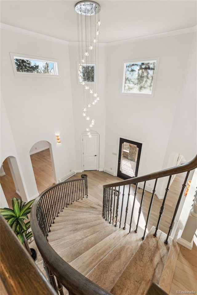 staircase featuring arched walkways, a high ceiling, wood finished floors, baseboards, and ornamental molding