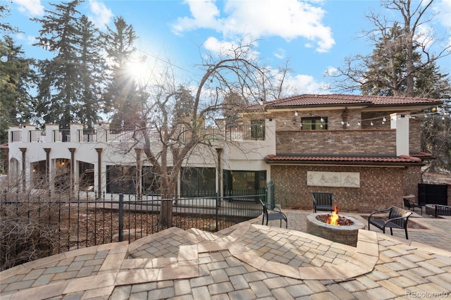 back of property featuring a tiled roof, a patio area, a fire pit, and a balcony