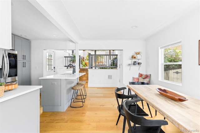 kitchen with a breakfast bar, light countertops, gray cabinets, stainless steel fridge, and light wood finished floors