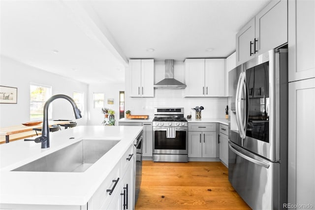 kitchen featuring stainless steel appliances, wall chimney range hood, a sink, light countertops, and light wood-type flooring