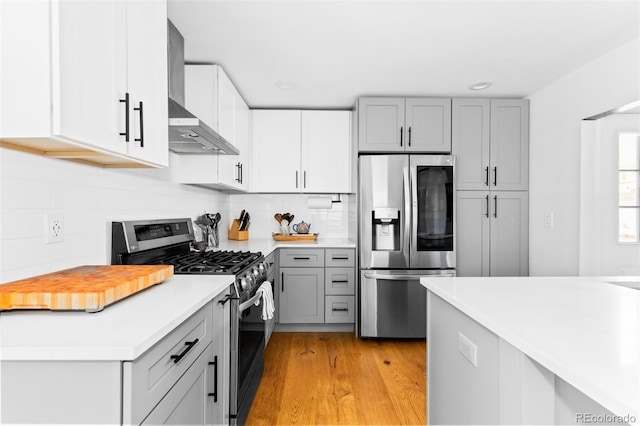 kitchen with stainless steel appliances, gray cabinetry, wall chimney exhaust hood, light wood finished floors, and light countertops