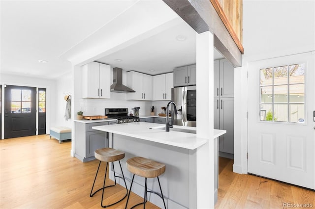 kitchen with wall chimney exhaust hood, appliances with stainless steel finishes, gray cabinets, light countertops, and a breakfast bar area