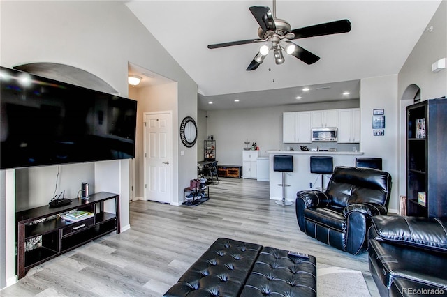 living area featuring lofted ceiling, baseboards, ceiling fan, and light wood finished floors