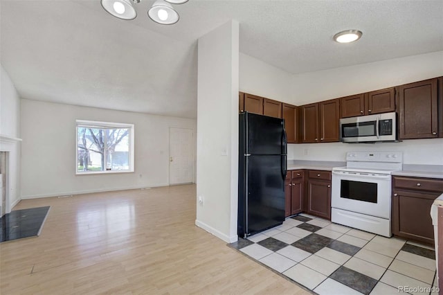 kitchen featuring light countertops, freestanding refrigerator, electric stove, stainless steel microwave, and vaulted ceiling