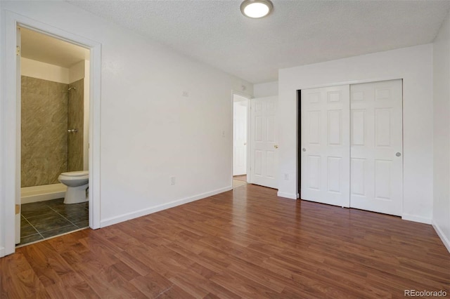 unfurnished bedroom with a closet, baseboards, ensuite bathroom, a textured ceiling, and wood finished floors