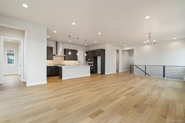 interior space featuring a sink, open floor plan, wall chimney range hood, tasteful backsplash, and a chandelier