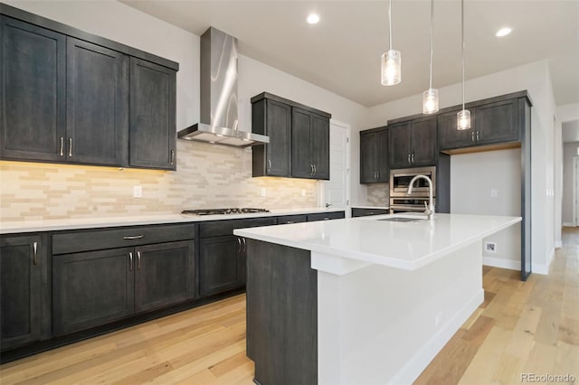 kitchen with a sink, wall chimney exhaust hood, light wood finished floors, and stainless steel appliances