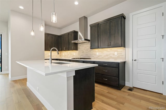 kitchen with a sink, light wood-type flooring, tasteful backsplash, and wall chimney range hood