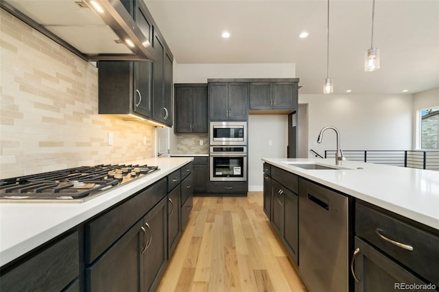 kitchen featuring stainless steel appliances, wall chimney exhaust hood, light countertops, and a sink