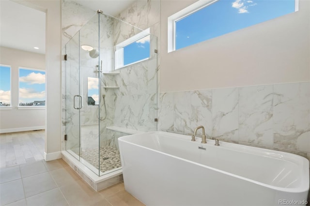 bathroom featuring a marble finish shower, tile patterned flooring, baseboards, a soaking tub, and tile walls